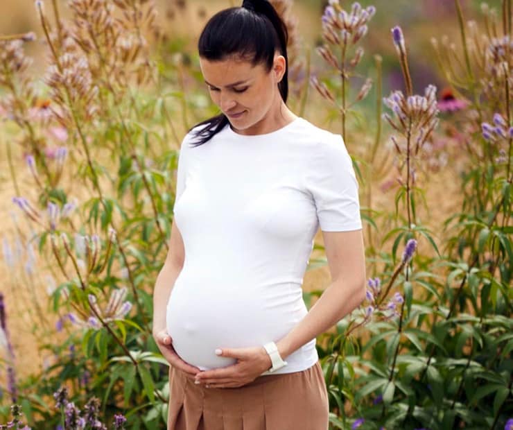 Pregnant women standing in a flower field holding her belly. | Fertility Cleanse Detox